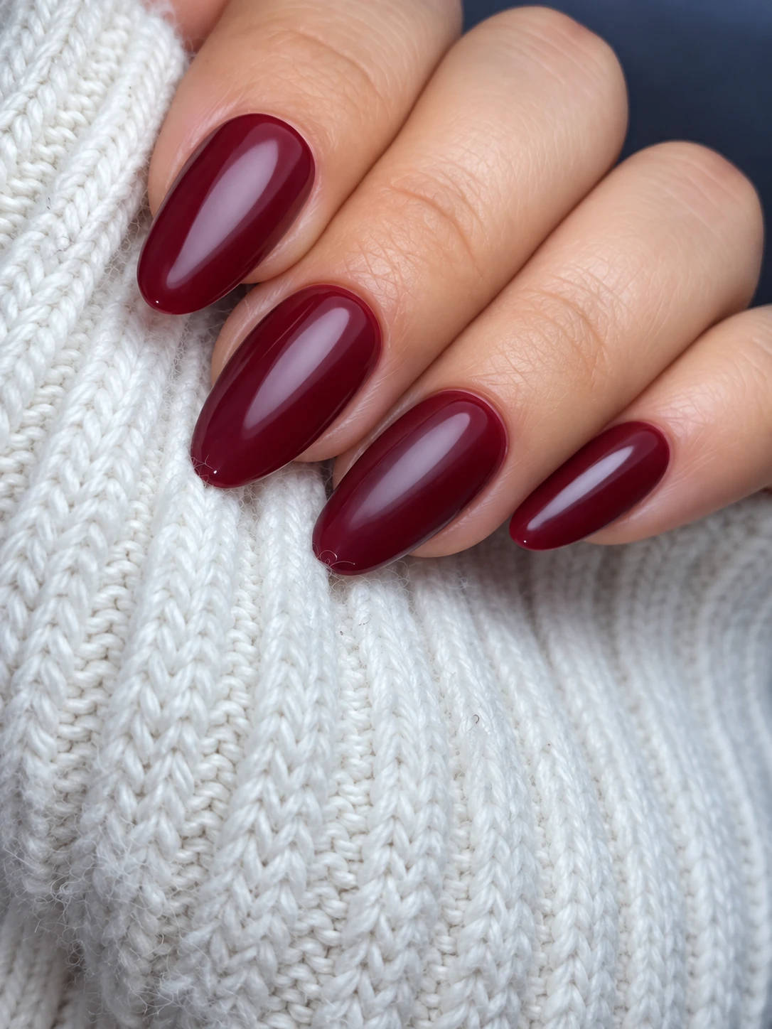 Glossy burgundy oval nails against ivory knitted fabric.
